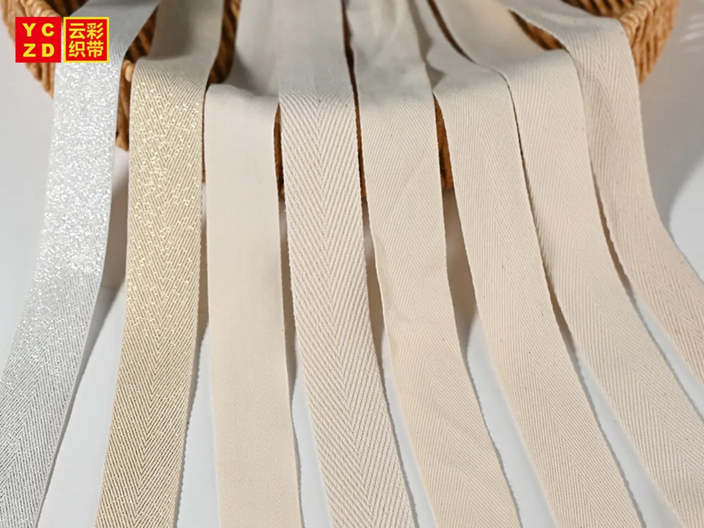 Várias fitas de tecido creme e branco com padrões de superfície lisos, diagonais e em espinha, dispostas sobre uma cesta