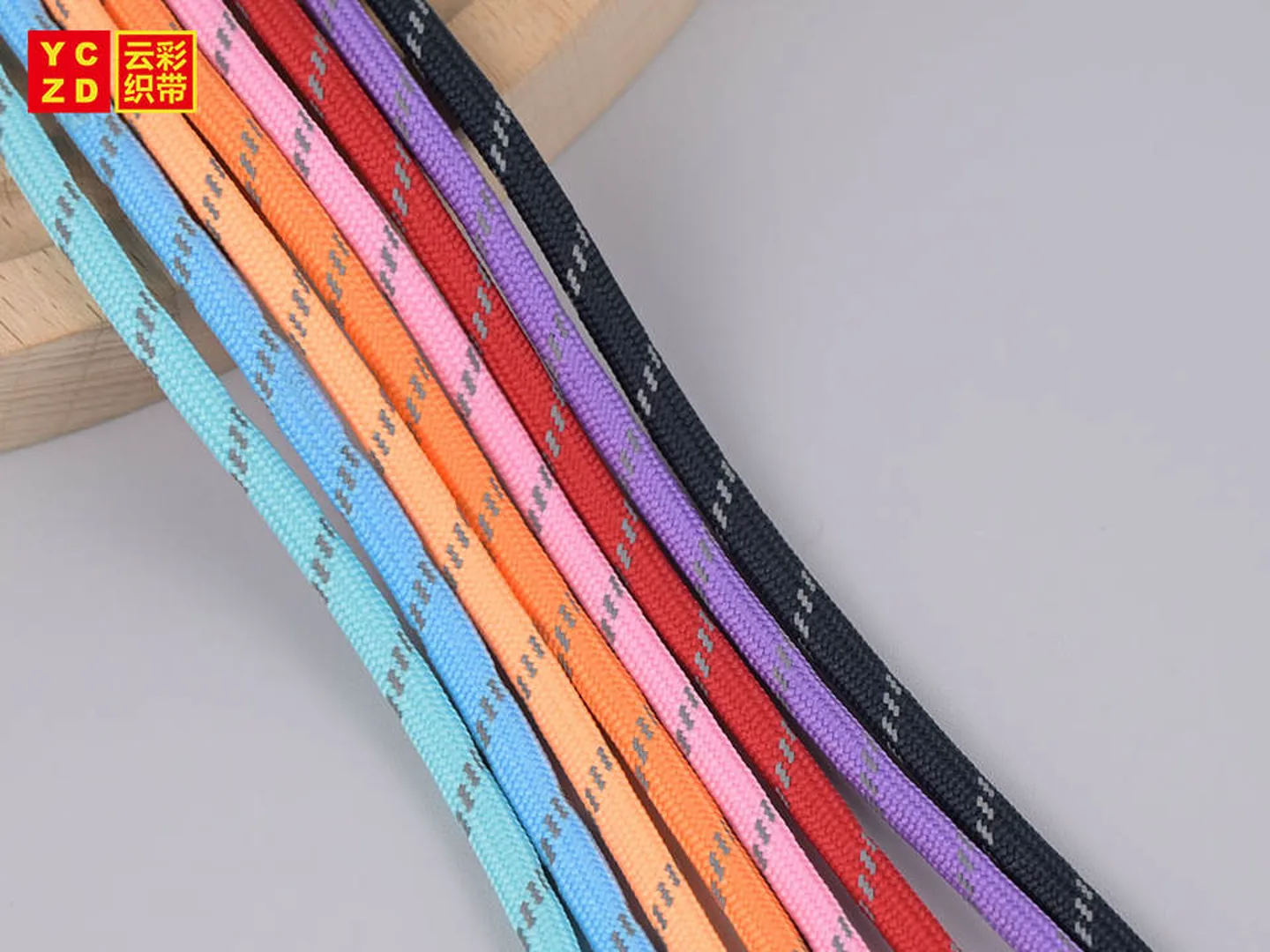 Blaue, orangefarbene, rosafarbene, rote, violette und schwarze Flechtkordeln mit grauen Musterdetails über einer Holzstrebe