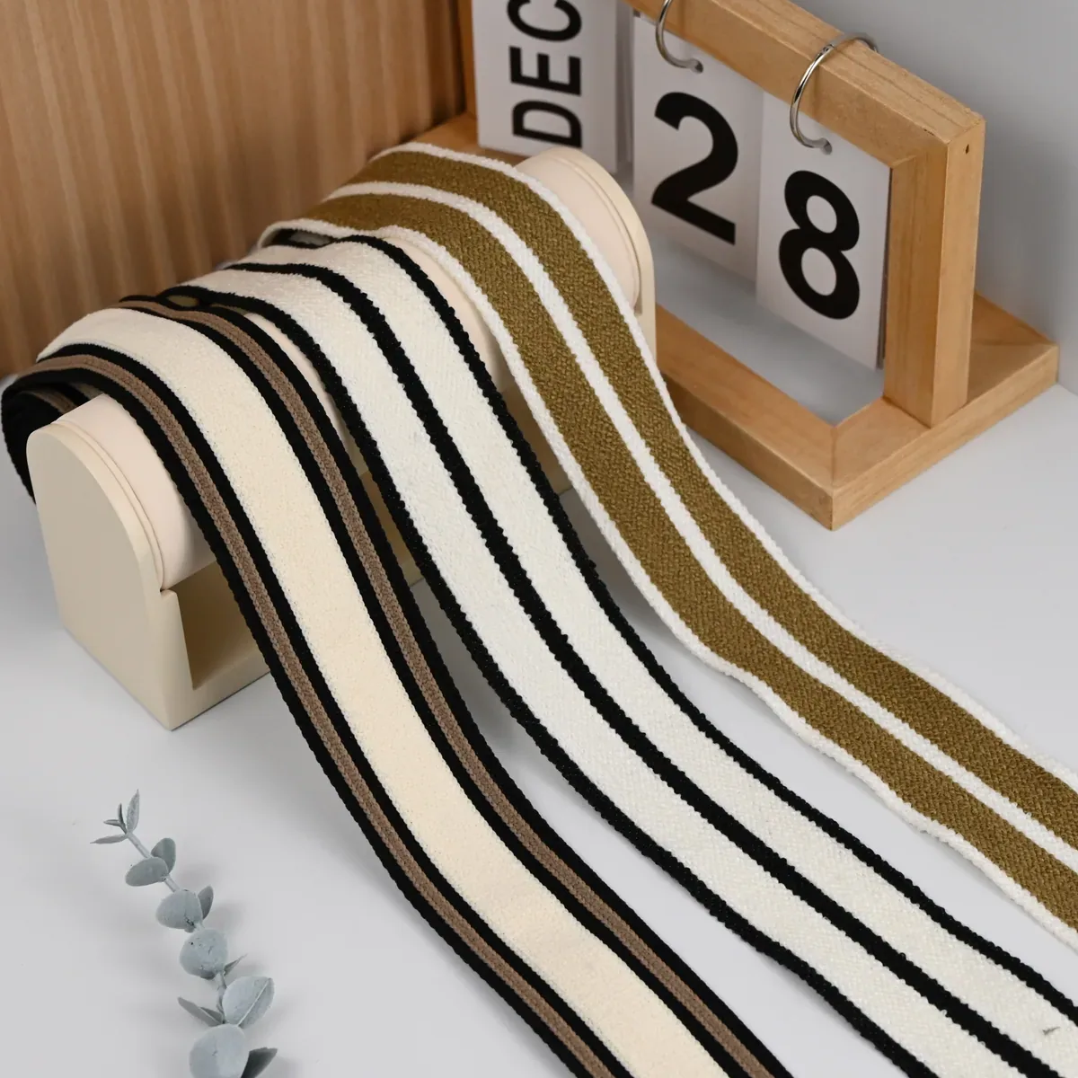 Cream knitted tapes with black and olive stripes draped over a display stand